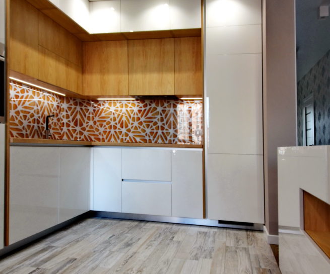 Сучасна кутова кухня з білими глянцевими фасадами, дерев'яними верхніми шафами та акцентним скляним скіналі з помаранчевим графічним візерунком