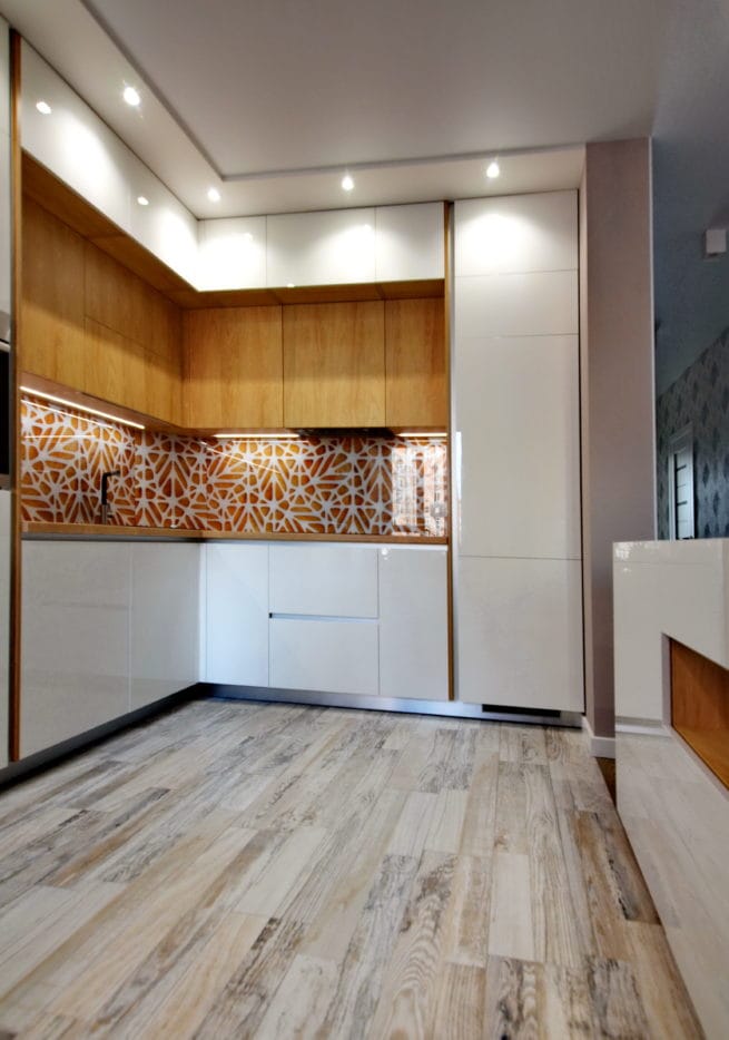 Сучасна кутова кухня з білими глянцевими фасадами, дерев'яними верхніми шафами та акцентним скляним скіналі з помаранчевим графічним візерунком